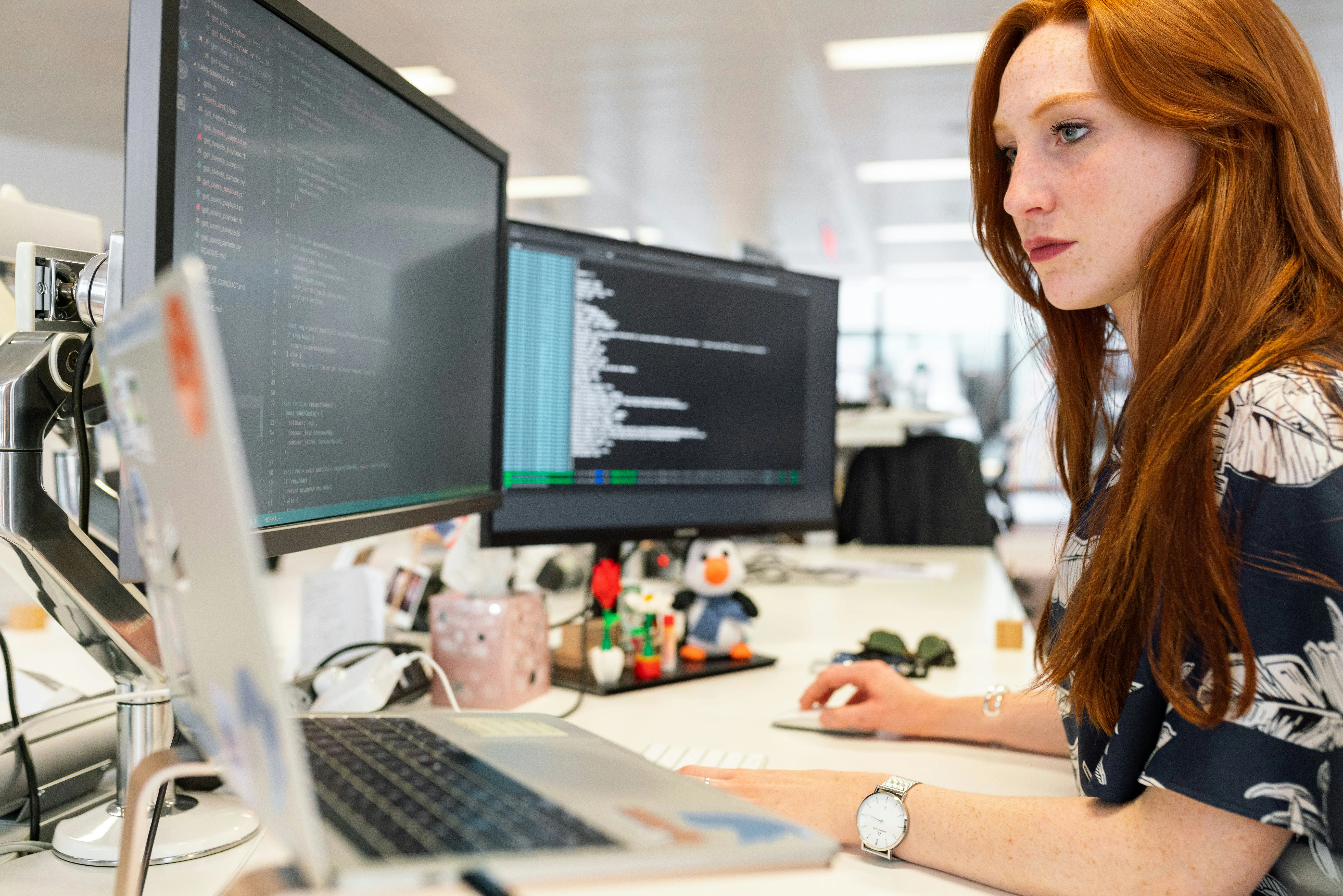 Software engineer reviewing code on dual monitors at her desk